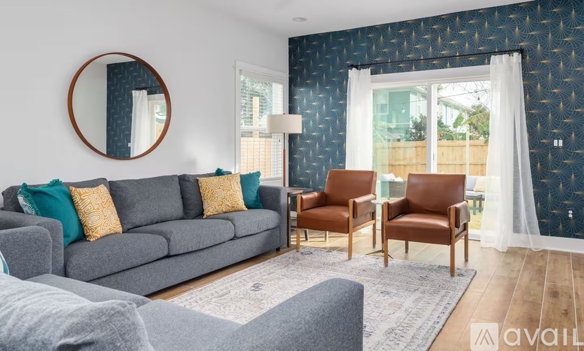 A living room with a grey sofa, two chairs and a round mirror on the wall.