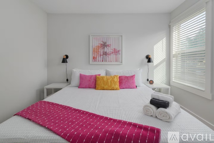 A bedroom with a white bed and a pink and yellow pillow.