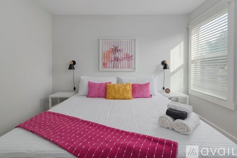 A bedroom with a white bed and a pink and yellow pillow.