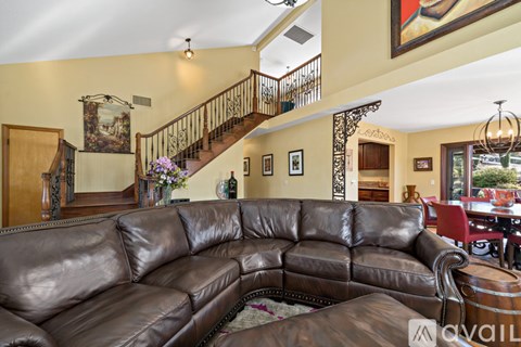 A brown leather couch in a living room with a staircase in the background.