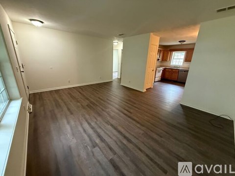 A spacious room with wooden flooring and a view of a kitchen in the distance.