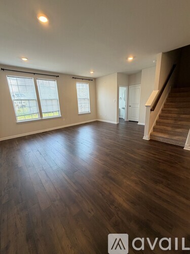 A spacious room with wooden floors and a staircase leading to another level.