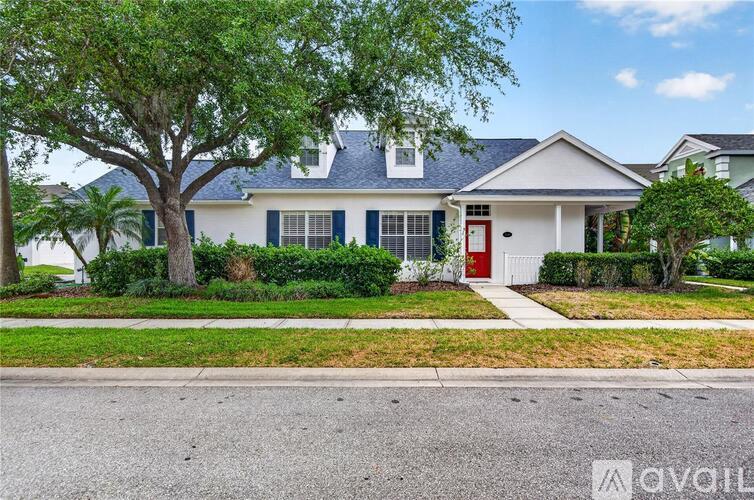 A white house with a red door and green trees in front.
