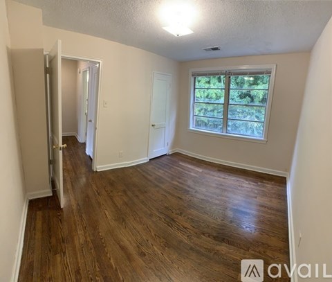 A room with wooden flooring and a window showing greenery outside.