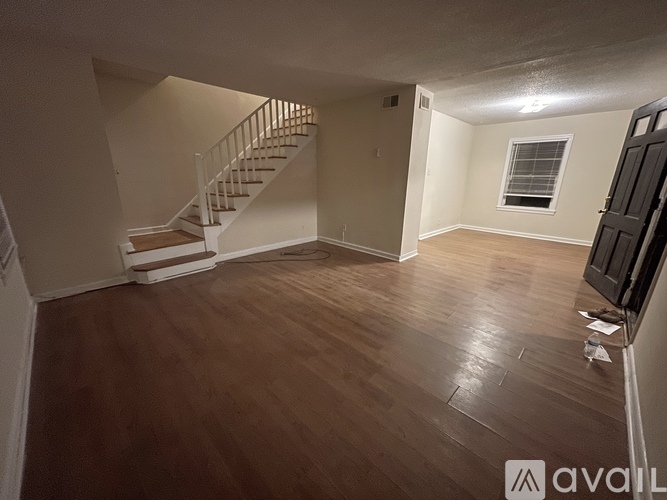 A spacious room with wooden flooring and a staircase.