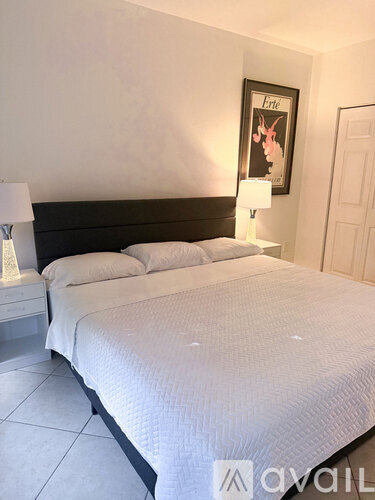A bed with a white comforter and two pillows sits in a room with a poster on the wall.