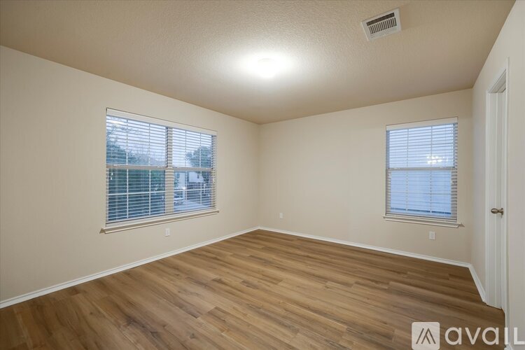 A room with wooden flooring and two windows with blinds.