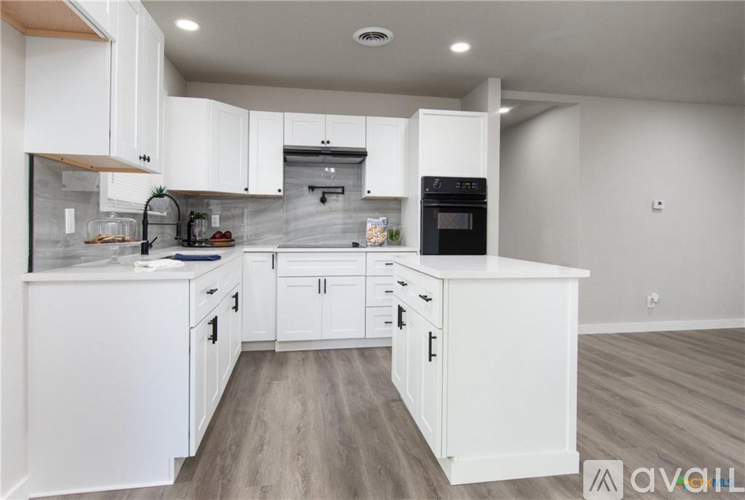 A modern kitchen with white cabinets and a wooden floor.