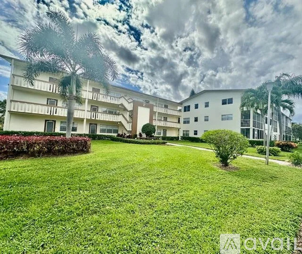A large grassy area in front of a building with a tree and bushes.