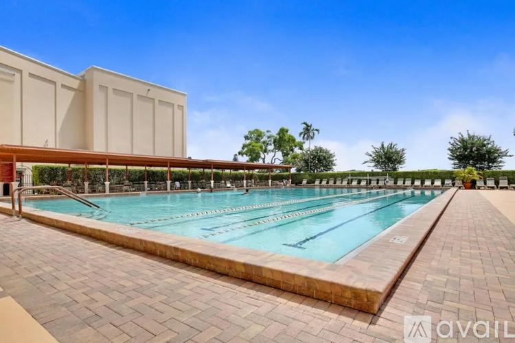 A large outdoor swimming pool surrounded by a brick patio and a building with a red roof.
