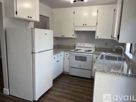 A white refrigerator is in a kitchen with white cabinets.