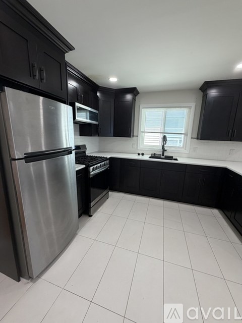 A kitchen with black cabinets and a stainless steel refrigerator.