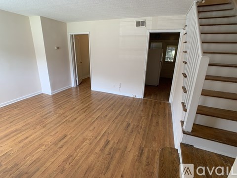 A room with wooden floors and a staircase on the right side.