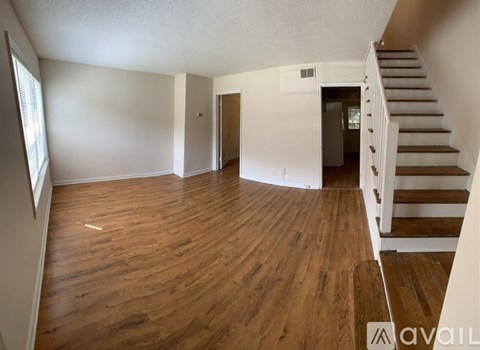 A spacious room with wooden floors and a staircase leading to another room.