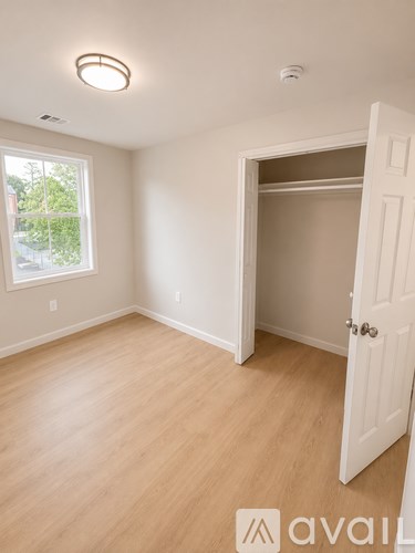 A room with a white door and a window with a view of trees outside.