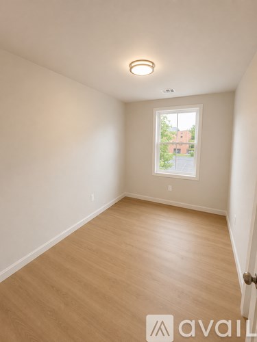 A room with wooden flooring and a window showing a view of a building and trees.