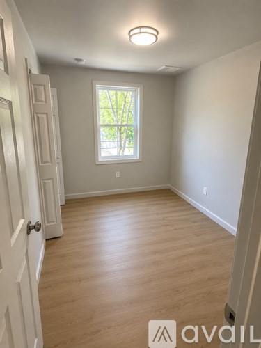 A room with a white door and a window with a view of trees.
