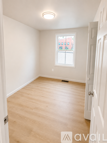 A room with a white door and a window with a view of a red building.