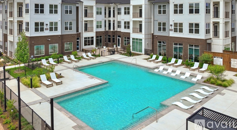 A large swimming pool surrounded by lounge chairs in front of apartment buildings.