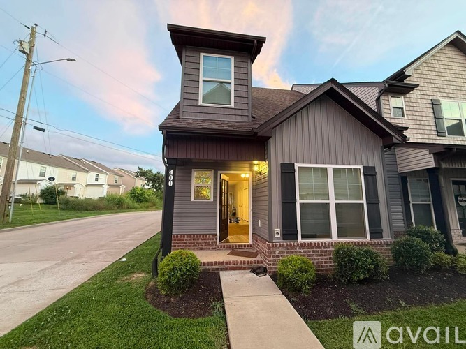 A house with a brown roof and a front yard with bushes and a walkway leading to the front door.