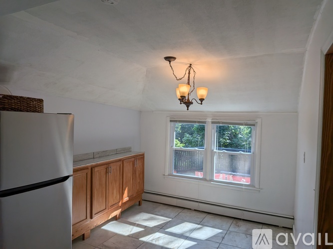 A kitchen with a fridge, wooden cabinets and a window.