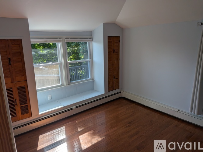 A room with wooden floors and a large window with a view of trees and a fence.