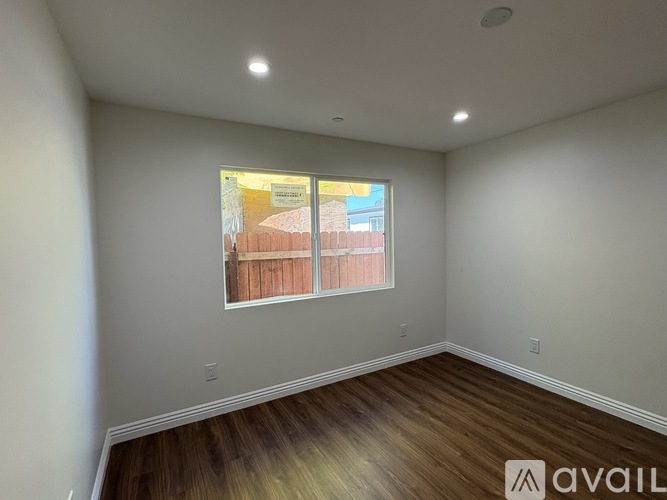 A room with a window showing a view of a fence and a building outside.