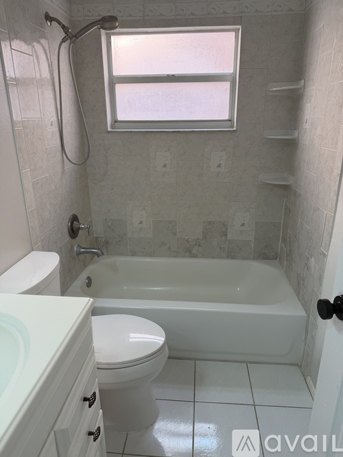 A white bathroom with a toilet, tub, and window.