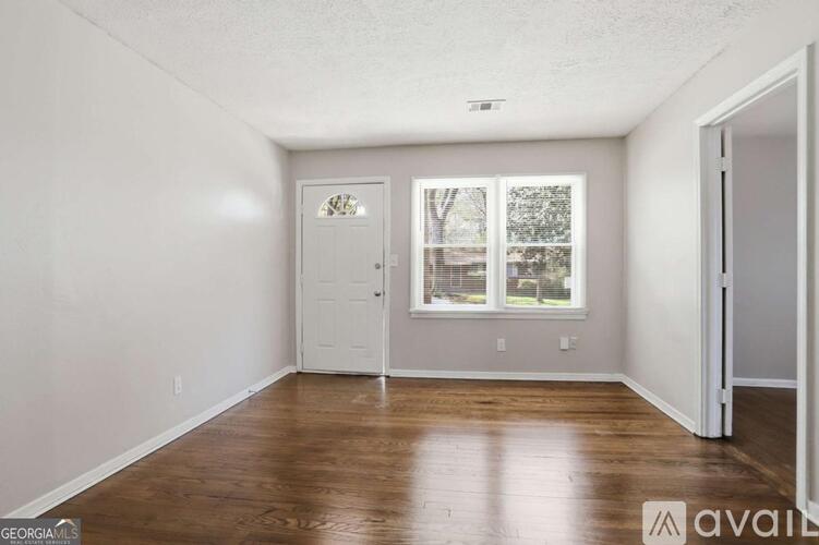 A room with wooden floors and a window showing trees outside.