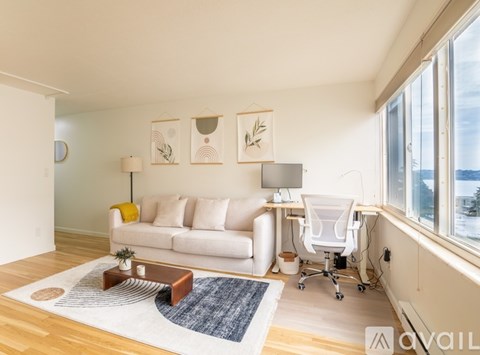 A living room with a white couch, a desk with a chair, and a rug on the floor.