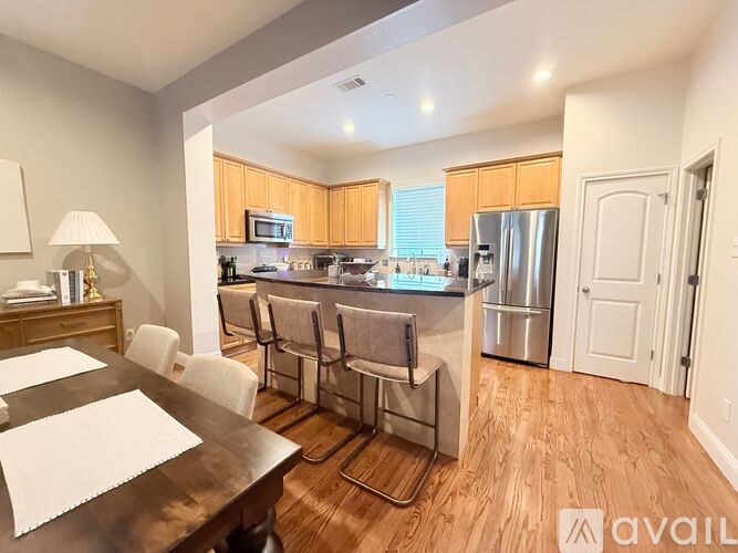 A kitchen with a dining table and chairs in the foreground and a refrigerator in the background.