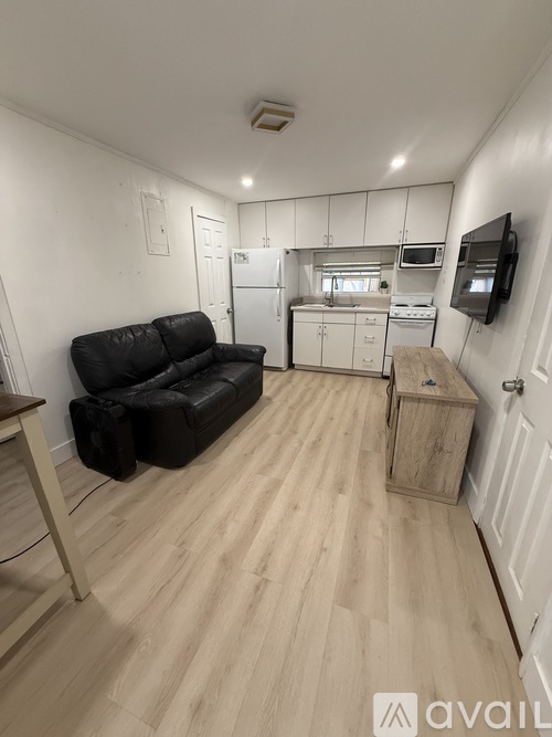 A black leather couch sits in a kitchen with wooden floors and white walls.