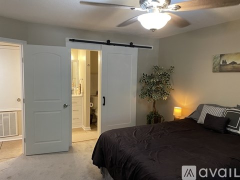 A bedroom with a bed, ceiling fan, and a door leading to a hallway.