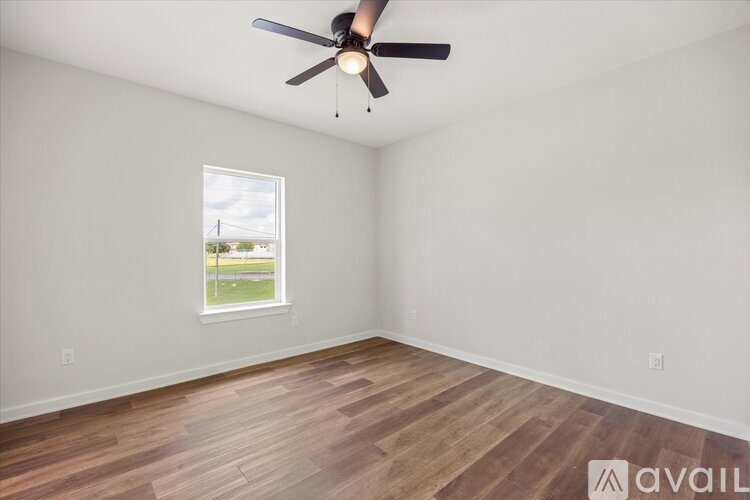 A room with a ceiling fan and a window showing a view of a grassy field.