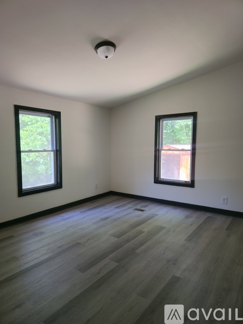 A room with wooden flooring and two windows.