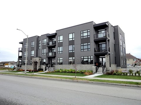 A grey apartment building with balconies and a front yard.