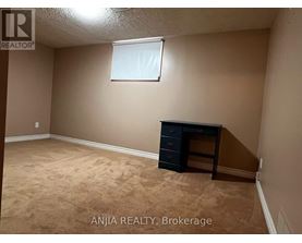 A room with beige walls and carpeting, a window, and a black dresser.