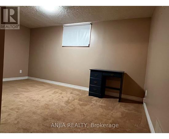 A room with beige walls and carpeting, a window, and a black dresser.