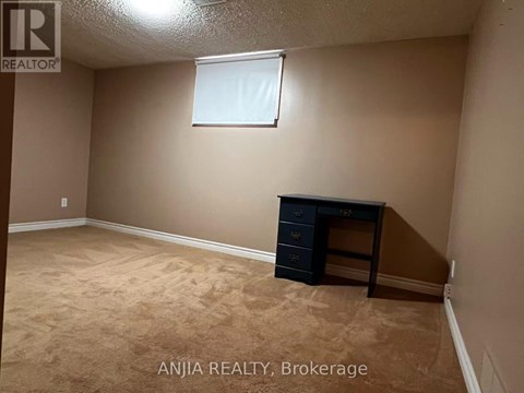 A room with beige walls and carpeting, a window, and a black dresser.