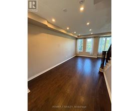 A spacious room with wooden floors and a staircase on the right side.