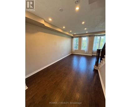 A spacious room with wooden floors and a staircase on the right side.