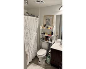 A white toilet in a small bathroom with a shower curtain and a shelf with various items on it.