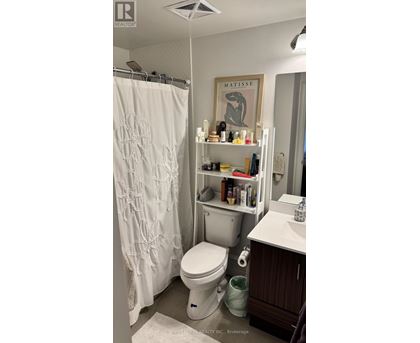 A white toilet in a small bathroom with a shower curtain and a shelf with various items on it.