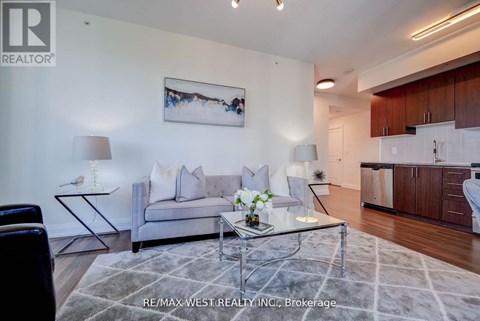 A living room with a grey couch, a glass coffee table, and a painting on the wall.