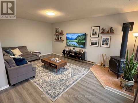 A living room with a grey couch, a coffee table, a flat screen TV, and a wood burning stove.