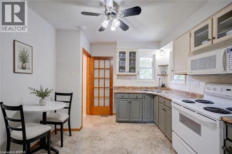 A kitchen with a white stove top oven and a white ceiling fan.