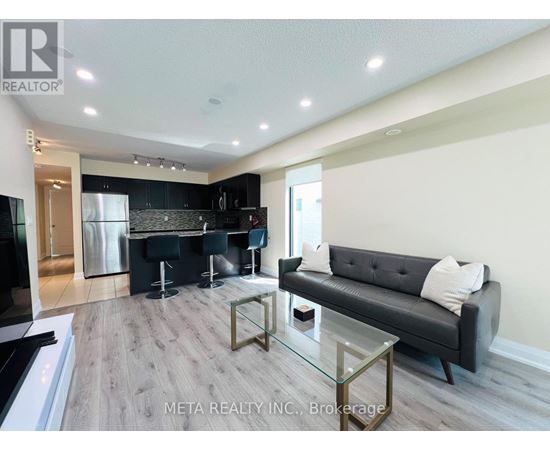 A modern kitchen with a black couch and a glass table.