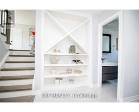 A white shelving unit with various decorative items is in a room with a staircase.