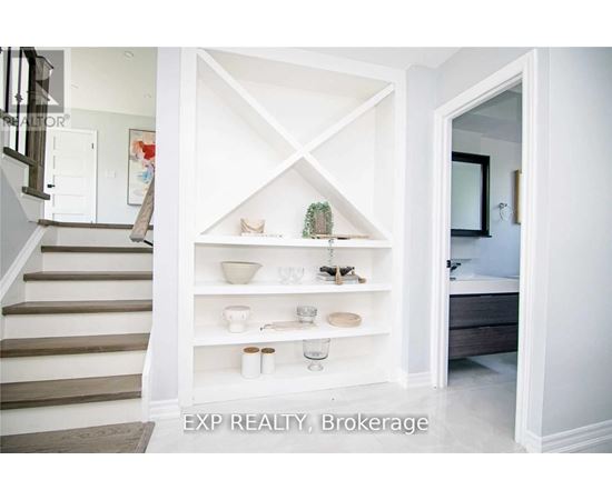 A white shelving unit with various decorative items is in a room with a staircase.