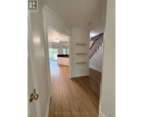 A hallway with a wooden floor and a staircase with white railings.